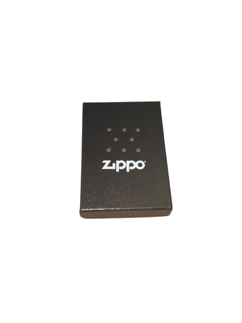 Puede incluir: Una caja de encendedor Zippo gris oscuro con una superficie texturizada. La caja tiene un patr&oacute;n de nueve puntos peque&ntilde;os y espaciados uniformemente y el logotipo blanco de Zippo. La caja es rectangular y tiene un borde ligeramente elevado.