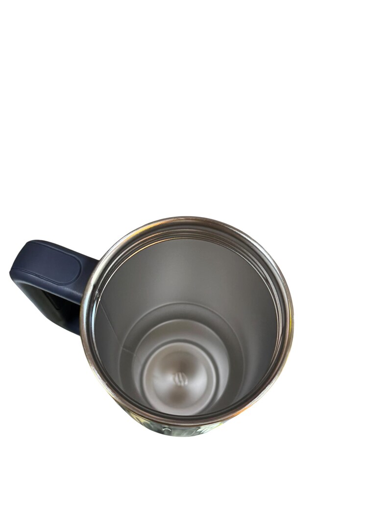May include: A stainless steel travel mug with a dark blue handle. The interior of the mug is silver, and the rim is a shiny silver color. The mug is empty and appears to be clean.