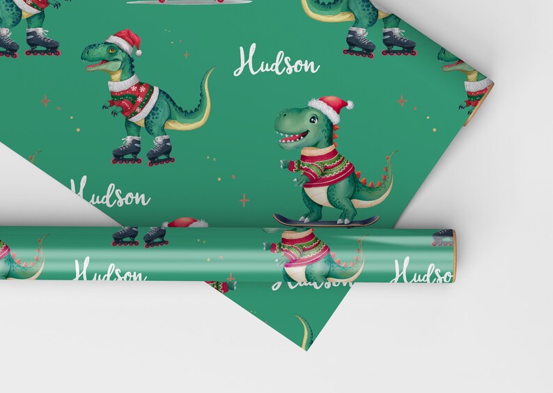 May include: Green wrapping paper with a repeating pattern of dinosaurs wearing Santa hats and roller skating. The dinosaurs are green with red and white sweaters. The text "Hudson" is repeated on the paper.