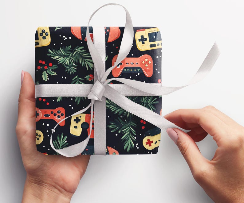K&ouml;nnte beinhalten: Ein Geschenk, verpackt mit einem schwarzen Hintergrund, der mit roten und gelben Gamecontrollern, gr&uuml;nen Zweigen und wei&szlig;en Punkten gemustert ist. Das Geschenk ist mit einem wei&szlig;en Band und einer Schleife gebunden.