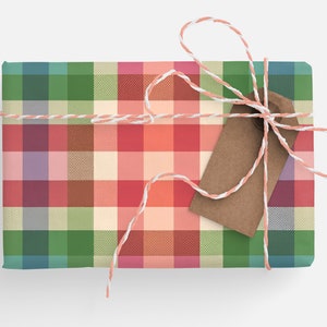 May include: A wrapped gift with a colorful plaid pattern in shades of green, red, pink, and beige. The gift is tied with a white and peach-colored twine and a brown paper tag.
