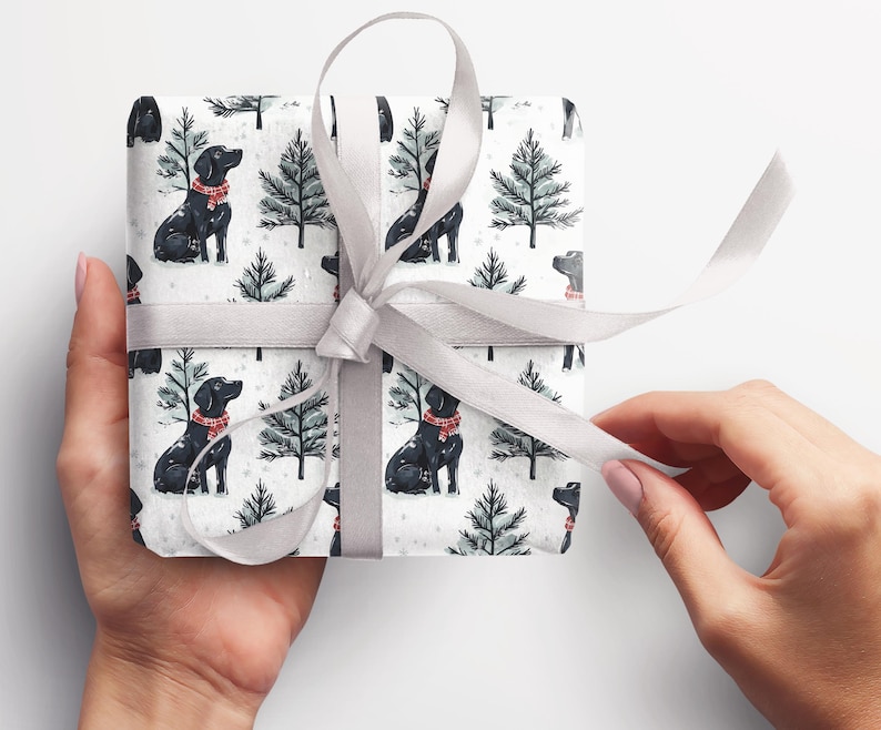 K&ouml;nnte beinhalten: Ein verpacktes Geschenk mit wei&szlig;em Hintergrund. Das Geschenkpapier zeigt ein Muster aus schwarzen Hunden mit roten Schals und gr&uuml;nen Weihnachtsb&auml;umen auf wei&szlig;em Grund. Ein silbernes Band ist um das Geschenk gebunden.