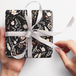 Op de afbeelding: Een cadeau verpakt in zwart-witte bloemenprint inpakpapier met een wit satijnen lint.