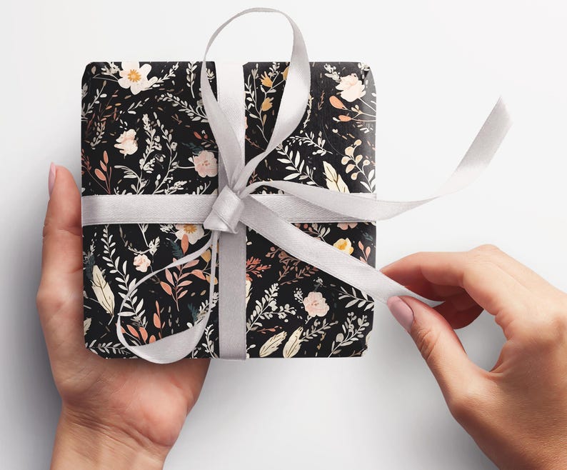 Op de afbeelding: Een cadeau verpakt in zwart-witte bloemenprint inpakpapier met een wit satijnen lint.