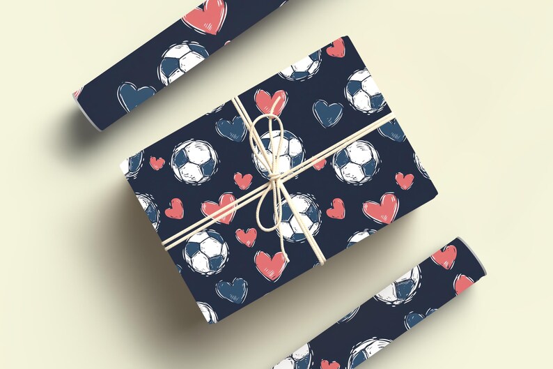 K&ouml;nnte beinhalten: Zwei Rollen Geschenkpapier mit dunkelblauem Hintergrund und einem Muster aus wei&szlig;en Fu&szlig;b&auml;llen und rosa Herzen.