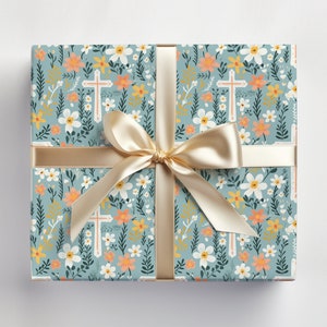 May include: A blue gift wrap with a floral pattern featuring white flowers, green leaves, and orange and yellow accents. The pattern also includes white crosses. The gift wrap is tied with a gold ribbon.
