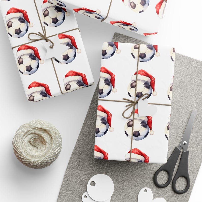 May include: White wrapping paper with a repeating pattern of soccer balls wearing Santa hats. The paper is tied with twine and a white gift tag.