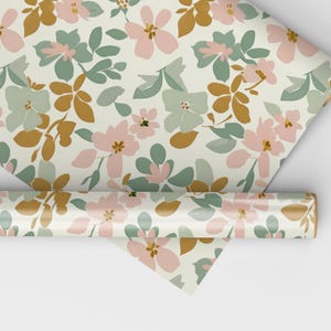 Op de afbeelding: Een rol cadeaupapier met een bloemenpatroon. Het papier heeft roze, groene en gouden bloemen op een cr&egrave;mekleurige achtergrond.