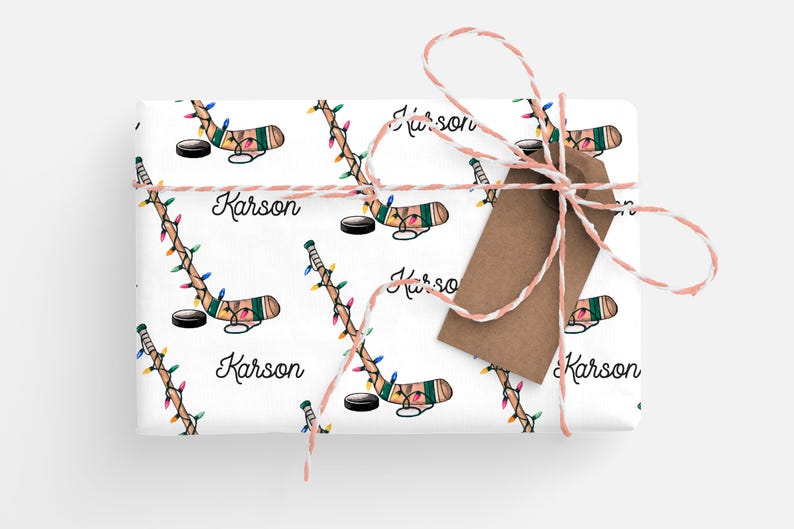 K&ouml;nnte beinhalten: Wei&szlig;es Geschenkpapier mit einem sich wiederholenden Muster aus Hockeyschl&auml;gern mit Weihnachtslichtern und dem Namen "Karson" auf jedem Schl&auml;ger. Das Papier ist mit einem braunen und wei&szlig;en Bindfaden gebunden.