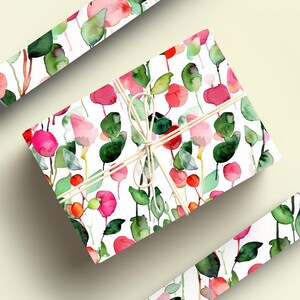 May include: A white gift wrap with a watercolor floral pattern featuring pink and red flowers and green leaves. The gift wrap is rolled up and tied with twine.