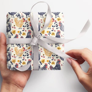Puede incluir: Un papel de regalo blanco con un patr&oacute;n repetitivo de pollos negros y amarillos y flores. El regalo est&aacute; atado con una cinta de sat&eacute;n blanca.