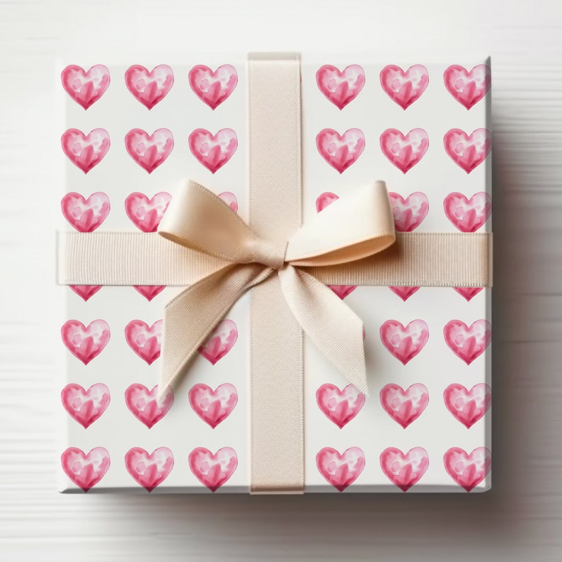 May include: A white gift box with a pink watercolor heart pattern and a beige satin ribbon tied in a bow.