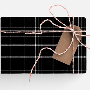 May include: A black and white plaid gift box tied with a white and pink twine bow. A brown gift tag is attached to the bow.