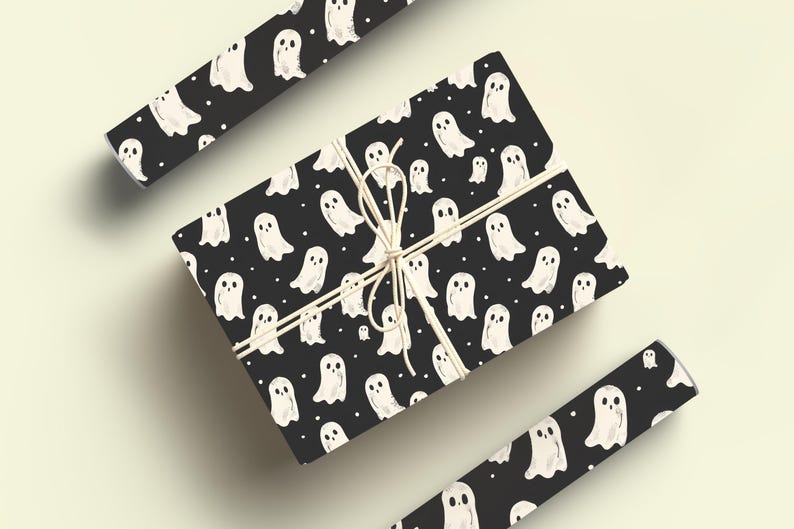 May include: A black gift box with a white ghost pattern wrapped with twine. The box is surrounded by rolls of wrapping paper with the same ghost pattern.