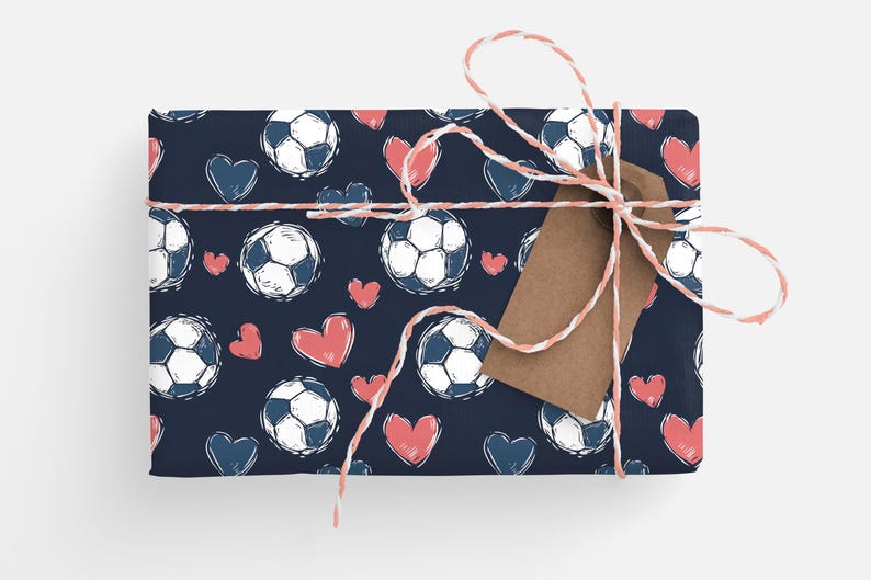 K&ouml;nnte beinhalten: Eine dunkelblaue Geschenkpapierrolle mit einem sich wiederholenden Muster aus wei&szlig;en Fu&szlig;b&auml;llen und rosafarbenen Herzen. Das Geschenk ist mit einem wei&szlig;en und roten Band und einem braunen Geschenkanh&auml;nger gebunden.