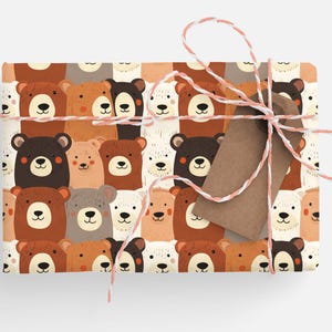 Op de afbeelding: Bruin en wit cadeaupapier met een herhalend patroon van cartoon beren gezichten. Het cadeaupapier is vastgebonden met wit en roze touw en een bruin cadeaukaartje.