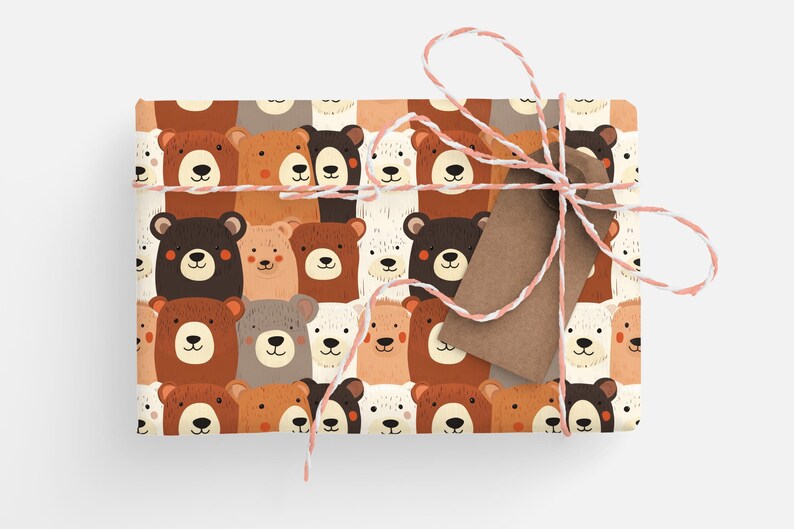 Op de afbeelding: Bruin en wit cadeaupapier met een herhalend patroon van cartoon beren gezichten. Het cadeaupapier is vastgebonden met wit en roze touw en een bruin cadeaukaartje.