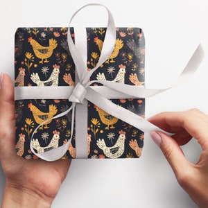 May include: A gift box wrapped in black and white wrapping paper with a pattern of colorful chickens and flowers. The box is tied with a white ribbon.