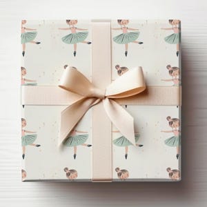 May include: A white gift box with a beige ribbon tied in a bow. The box is wrapped in wrapping paper with a pattern of little girls wearing green tutus and pink ballet shoes.