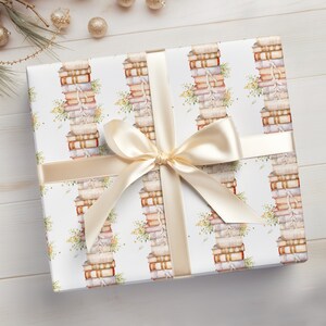May include: A white gift wrap with a repeating pattern of stacks of books with floral accents. The gift wrap is tied with a cream-colored ribbon with a bow.