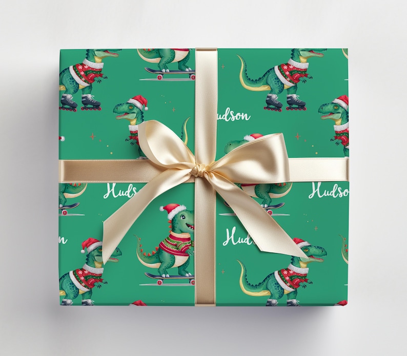 May include: Green wrapping paper with a repeating pattern of dinosaurs wearing Santa hats and riding skateboards. The paper is tied with a gold ribbon and the name "Hudson" is printed on the paper.
