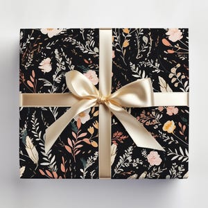 Op de afbeelding: Een zwarte cadeaudoos met een bloemenpatroon in roze, oranje en witte tinten. De doos is gebonden met een beige satijnen lint.