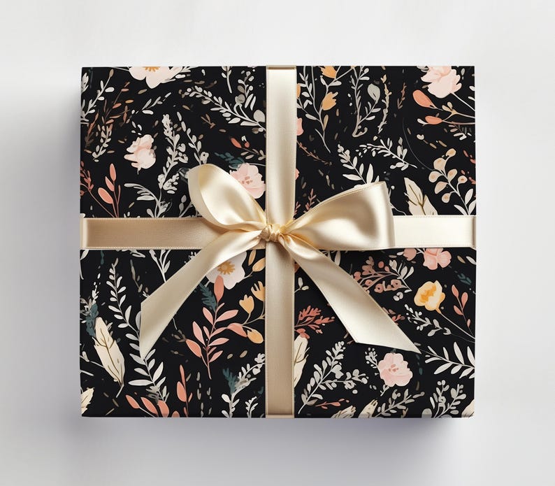 Op de afbeelding: Een zwarte cadeaudoos met een bloemenpatroon in roze, oranje en witte tinten. De doos is gebonden met een beige satijnen lint.