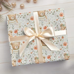May include: A white gift wrap with a beige ribbon bow. The wrapping paper features a repeating pattern of brown bears wearing sweaters, flowers, and leaves.