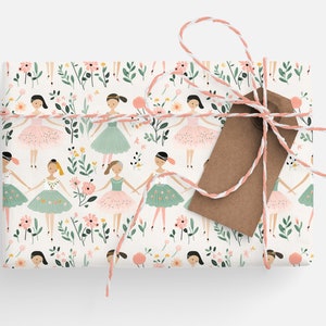 May include: A white gift wrap with a repeating pattern of ballerinas in pink and green tutus, surrounded by pink and green flowers. The gift is tied with a white and pink twine and a brown gift tag.