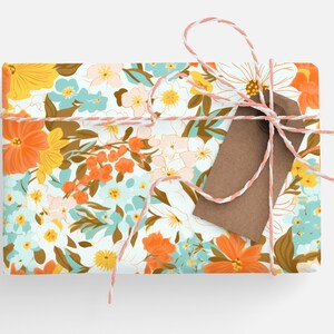May include: A gift box wrapped in floral patterned paper with a brown gift tag tied with white and pink twine. The paper features a white background with a repeating pattern of orange, yellow, blue, and brown flowers.