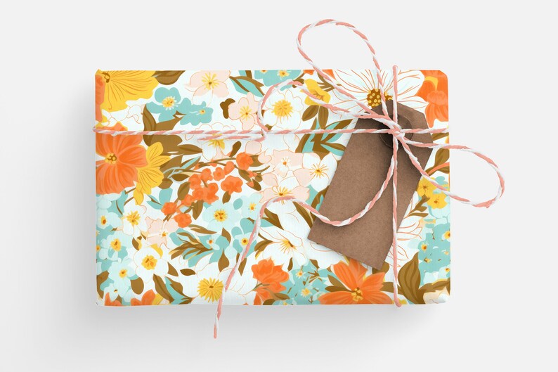 May include: A gift box wrapped in floral patterned paper with a brown gift tag tied with white and pink twine. The paper features a white background with a repeating pattern of orange, yellow, blue, and brown flowers.