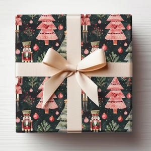 May include: A gift box wrapped in festive Christmas wrapping paper. The paper features a repeating pattern of pink Christmas trees, nutcracker figurines, and red and green ornaments on a dark green background. A cream-colored ribbon is tied around the box.