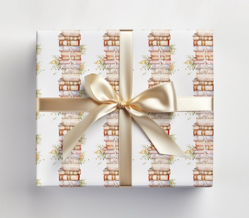 May include: White gift wrap with a repeating pattern of stacks of books and floral sprigs. A gold ribbon is tied around the box with a bow.