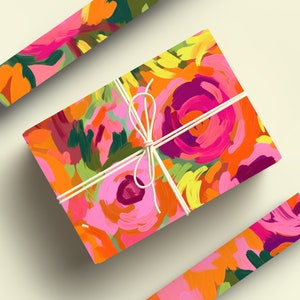 May include: A gift box wrapped in colorful floral patterned paper with a white ribbon. The paper features a bright pink, orange, yellow, and green abstract floral design.