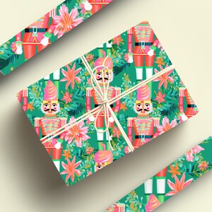 May include: Green and pink wrapping paper with a repeating pattern of nutcracker soldiers and tropical flowers. The paper is wrapped around a gift box with a white ribbon.