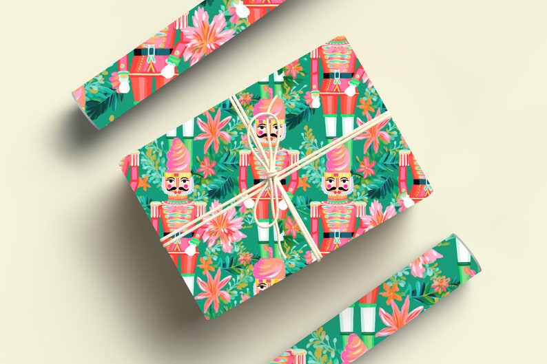 May include: Green and pink wrapping paper with a repeating pattern of nutcracker soldiers and tropical flowers. The paper is wrapped around a gift box with a white ribbon.