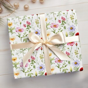 May include: A white gift box with a floral pattern featuring pink, yellow, and blue flowers. The box is tied with a cream-colored satin ribbon.