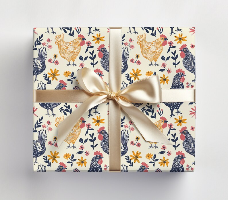 Puede incluir: Una caja de regalo envuelta en papel blanco con un patr&oacute;n repetitivo de pollos amarillos, flores rosas y hojas azules. Una cinta de color crema est&aacute; atada alrededor de la caja con un lazo.