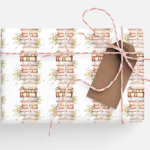 May include: A white gift box wrapped in a pattern of stacked books with floral accents. The box is tied with a pink and white twine bow and a brown gift tag.