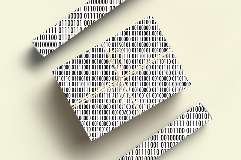 May include: Wrapping paper featuring a repeating pattern of black and white binary code. The wrapped gift is tied with string. Additional pieces of the same paper are scattered around the gift.