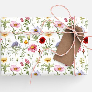 May include: A gift wrapped in white paper with a floral pattern. The paper features a variety of flowers in pink, red, yellow, and purple. The gift is tied with a pink and white twine and a brown gift tag.