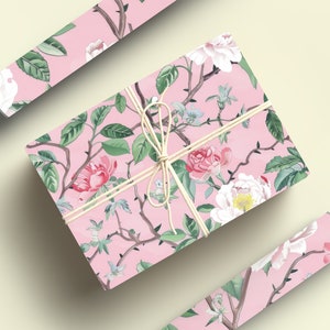May include: A wrapped gift box and two rolls of wrapping paper with a pink floral pattern. The design features pink and white flowers, green leaves, and brown branches. The box is tied with twine.