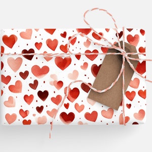 Op de afbeelding: Een witte cadeaudoos verpakt in rode en roze aquarelhartjes met een bruin cadeaukaartje en touw.
