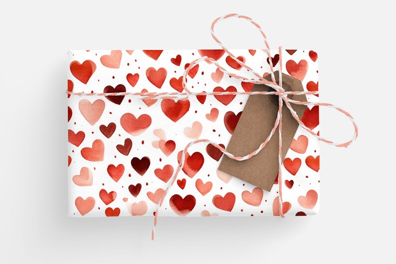 Op de afbeelding: Een witte cadeaudoos verpakt in rode en roze aquarelhartjes met een bruin cadeaukaartje en touw.