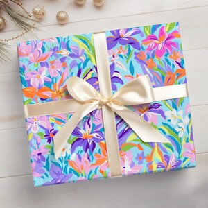 May include: A gift box wrapped in blue floral patterned paper with a large ivory satin bow. The paper features a colorful floral design with pink, orange, purple, and green flowers.