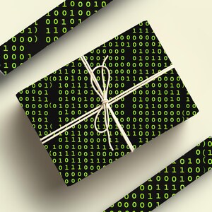 Peut inclure: Une bo&icirc;te cadeau emball&eacute;e et deux rouleaux de papier cadeau sont pr&eacute;sent&eacute;s. Le papier noir est recouvert d'un motif r&eacute;p&eacute;t&eacute; de code binaire vert. Le cadeau est nou&eacute; avec de la ficelle blanche sur un fond clair.