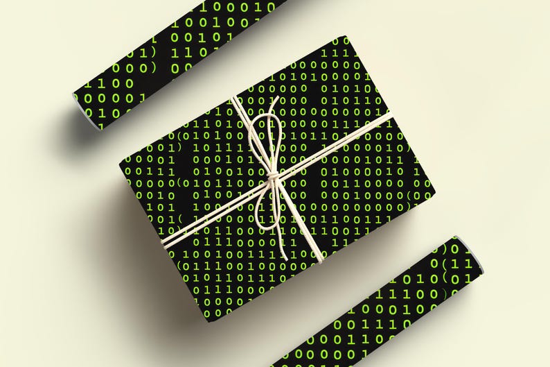 Peut inclure: Une bo&icirc;te cadeau emball&eacute;e et deux rouleaux de papier cadeau sont pr&eacute;sent&eacute;s. Le papier noir est recouvert d'un motif r&eacute;p&eacute;t&eacute; de code binaire vert. Le cadeau est nou&eacute; avec de la ficelle blanche sur un fond clair.