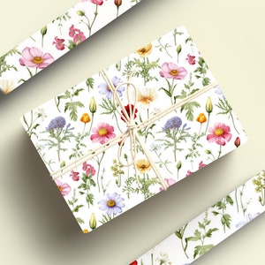 May include: A white gift box wrapped in floral patterned paper. The paper features a repeating pattern of pink, red, yellow, and blue flowers with green leaves. The box is tied with a natural twine bow.