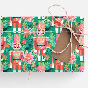 May include: Green wrapping paper with a repeating pattern of pink nutcracker soldiers and tropical flowers. The wrapping paper is tied with white and pink twine and a brown gift tag.