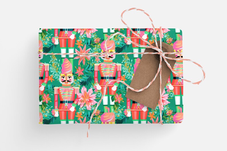 May include: Green wrapping paper with a repeating pattern of pink nutcracker soldiers and tropical flowers. The wrapping paper is tied with white and pink twine and a brown gift tag.